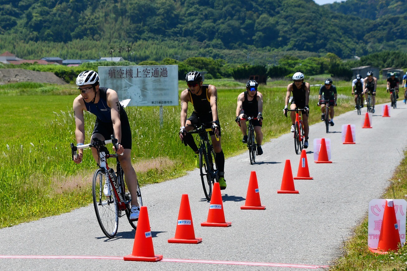選手在館山賽道自行車項目沿田間道路騎乘,路旁設有錐筒標示賽道