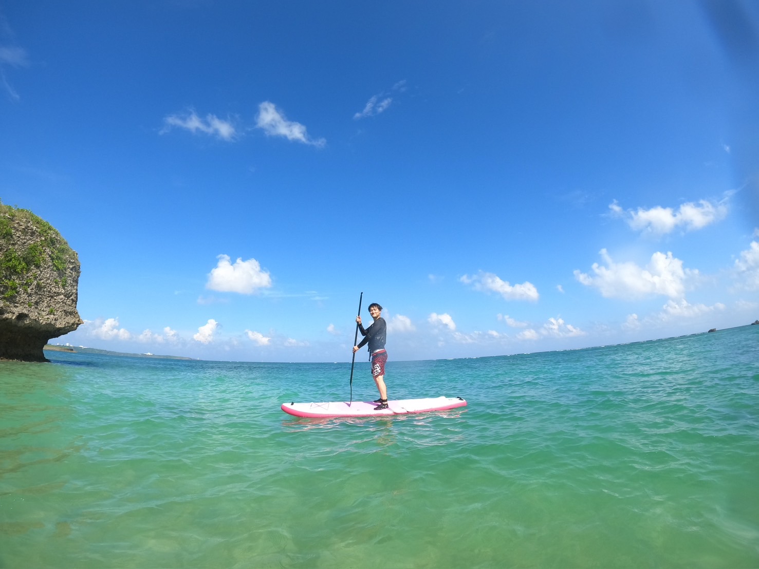 旅客於沖繩湛藍海域上站立划SUP立槳,遠方可見礁岩地形