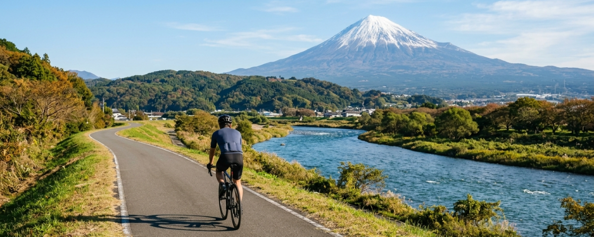 騎士騎行於靜岡伊豆狩野川專用單車道遠眺雄偉富士山（AI 生成示意圖）