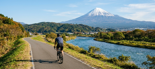 騎士騎行於靜岡伊豆狩野川專用單車道遠眺雄偉富士山（AI 生成示意圖）