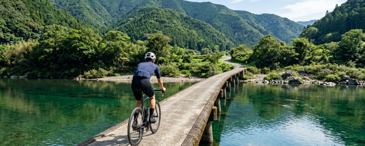 騎士騎行於高知四萬十川無欄杆水泥沈下橋遠眺碧綠清流與蒼翠山林（AI 生成示意圖）