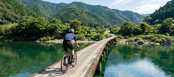 騎士騎行於高知四萬十川無欄杆水泥沈下橋遠眺碧綠清流與蒼翠山林（AI 生成示意圖）
